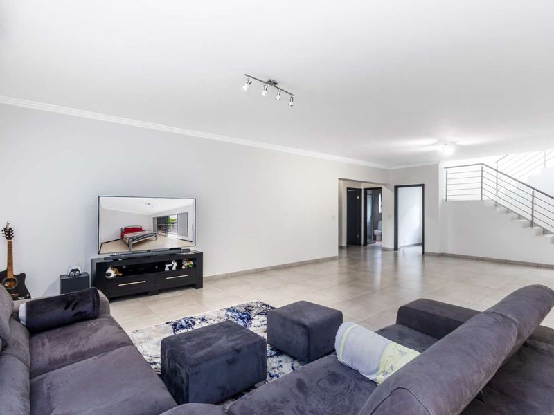 Spacious open-plan living area featuring neutral tiled flooring, a modern staircase with metal railings, and recessed ceiling lighting.