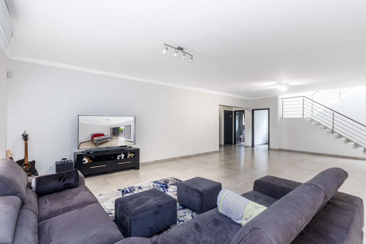 Spacious open-plan living area featuring neutral tiled flooring, a modern staircase with metal railings, and recessed ceiling lighting.