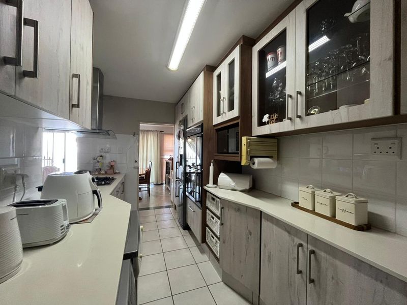 A well-maintained galley-style kitchen featuring modern built-in cabinetry, stone countertops, tiled flooring, and integrated appliances with ample storage space.