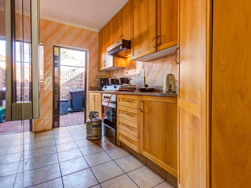 A functional kitchen featuring wooden cabinetry, granite countertops, a gas stove with extractor fan, and tiled finishes with direct access to an outdoor area.