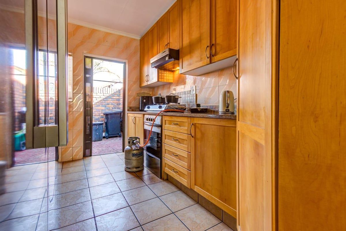 A functional kitchen featuring wooden cabinetry, granite countertops, a gas stove with extractor fan, and tiled finishes with direct access to an outdoor area.