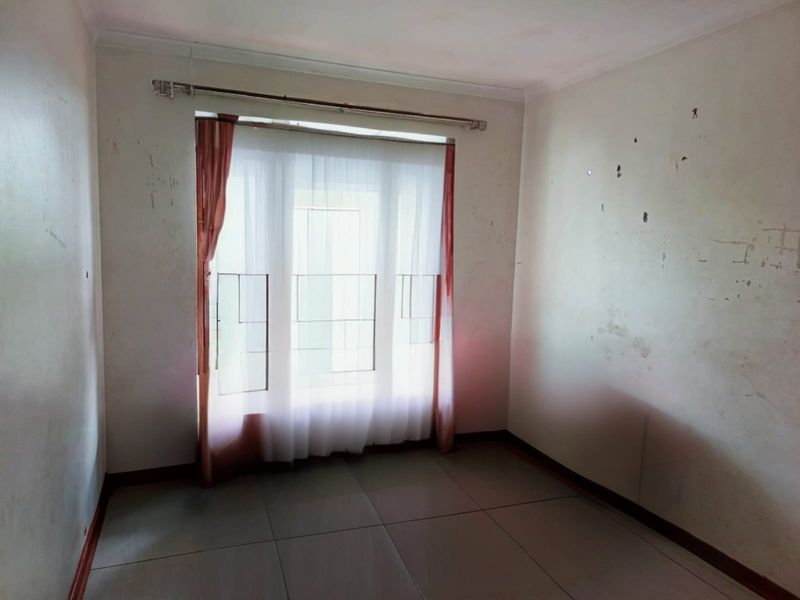 An empty bedroom featuring tiled flooring and a window with a curtain rod, requiring cosmetic wall repairs and repainting.