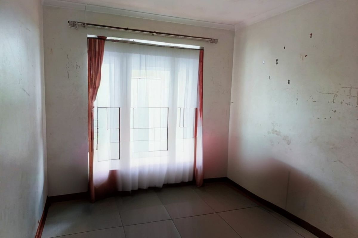 An empty bedroom featuring tiled flooring and a window with a curtain rod, requiring cosmetic wall repairs and repainting.