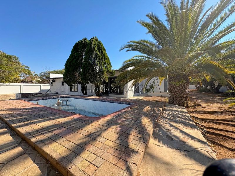 Rear garden area featuring an empty swimming pool with paved surround and boundary walling.