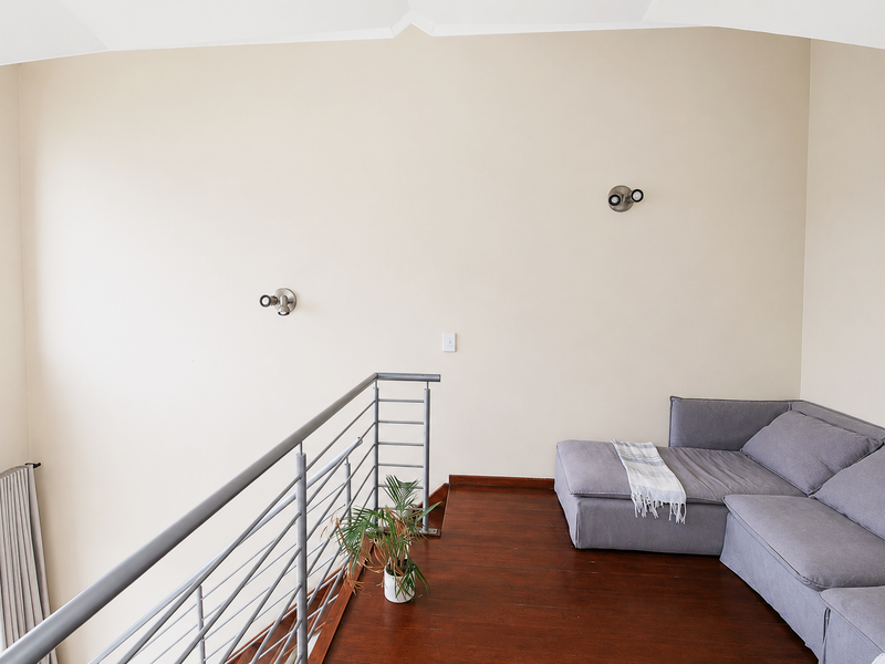 A mezzanine living area featuring hardwood flooring, a modern metal balustrade, and wall-mounted lighting, overlooking the lower level through a high-level window.