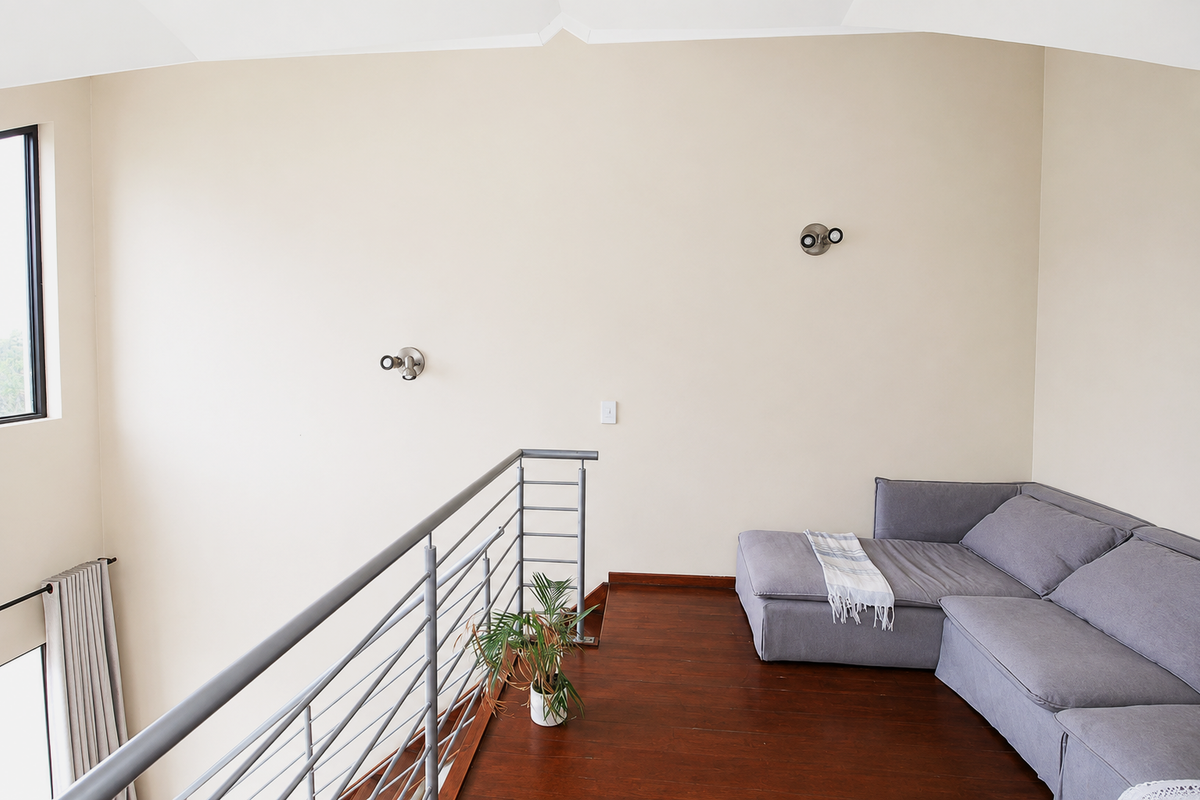 A mezzanine living area featuring hardwood flooring, a modern metal balustrade, and wall-mounted lighting, overlooking the lower level through a high-level window.