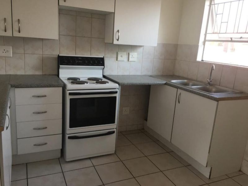 A functional kitchen featuring white cabinetry, laminate countertops, a double stainless steel sink, and a freestanding electric stove with tiled splashbacks.