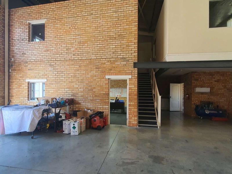 Spacious industrial-style utility area featuring exposed brick walls, concrete flooring, a staircase, and a steel support beam.