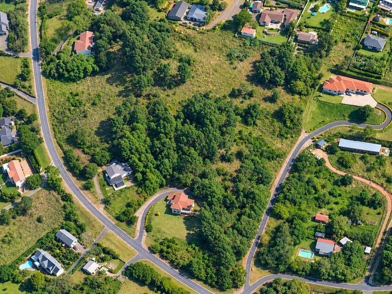 An aerial view of a residential area featuring vacant land plots, established trees, and paved access roads within a suburban neighborhood.