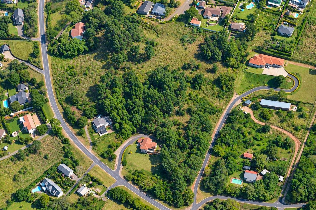 An aerial view of a residential area featuring vacant land plots, established trees, and paved access roads within a suburban neighborhood.