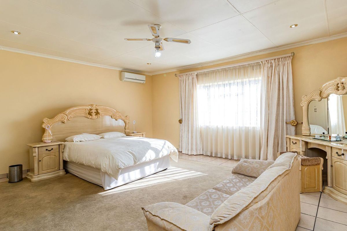 Spacious bedroom featuring neutral walls, carpeted flooring, a ceiling fan, and a wall-mounted air conditioning unit.