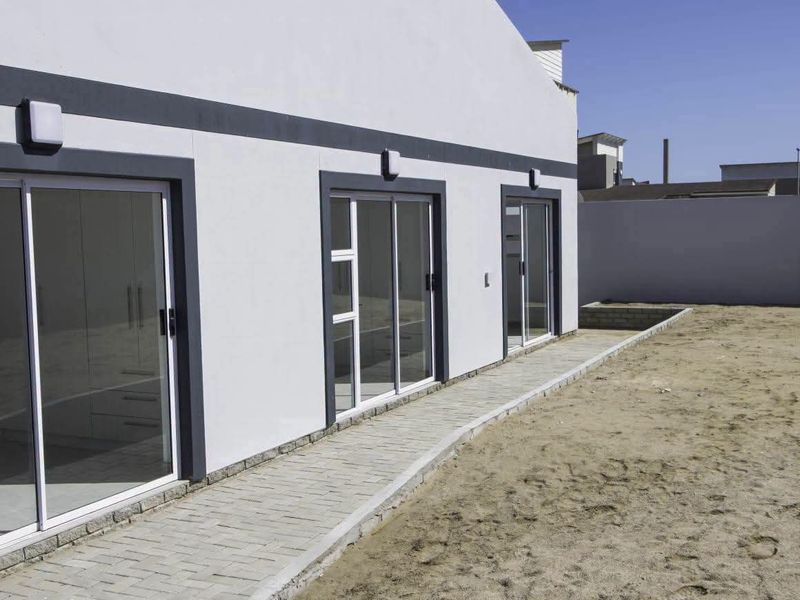 Rear exterior view of the property featuring a paved walkway, multiple sliding glass doors, and a clean, modern facade.