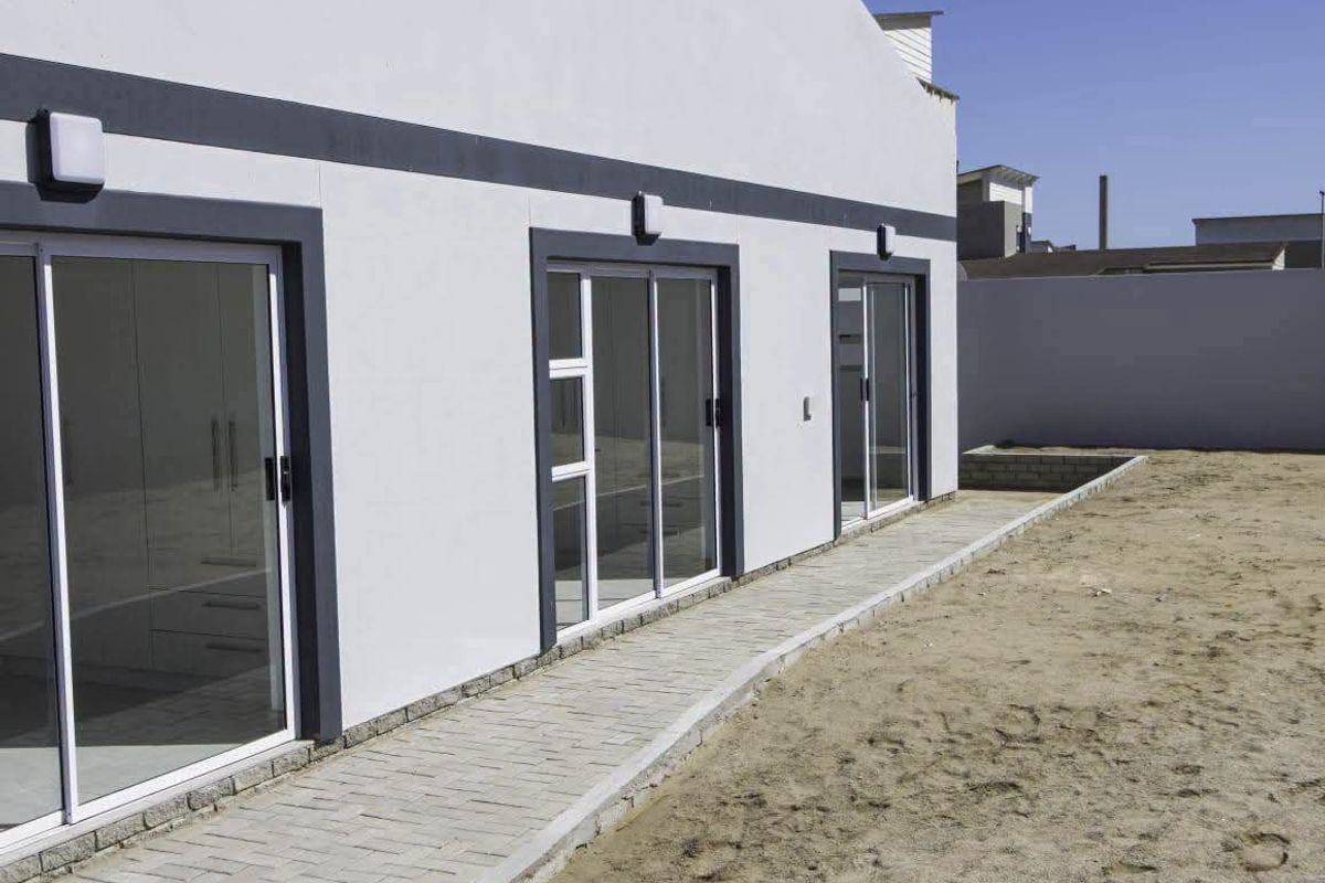 Rear exterior view of the property featuring a paved walkway, multiple sliding glass doors, and a clean, modern facade.