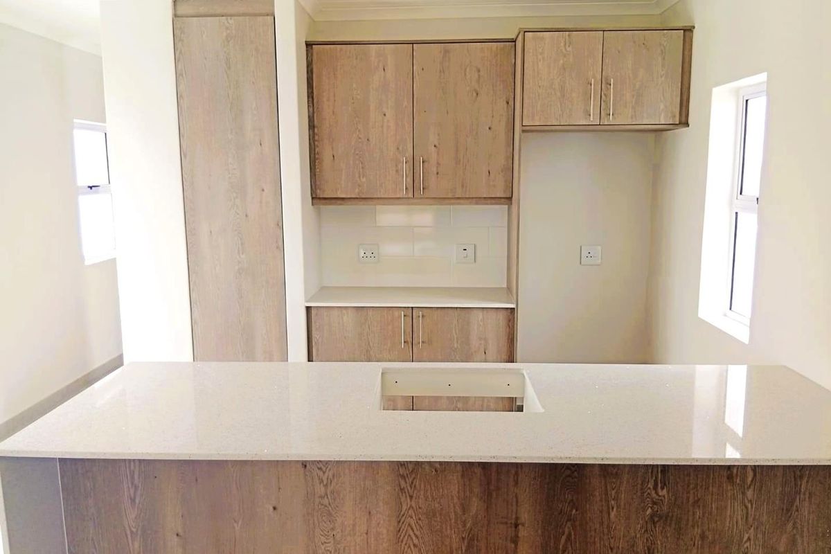 Modern kitchen featuring wood-grain cabinetry, stone countertops, and a tiled backsplash, offering a clean and functional space ready for final appliance installation.