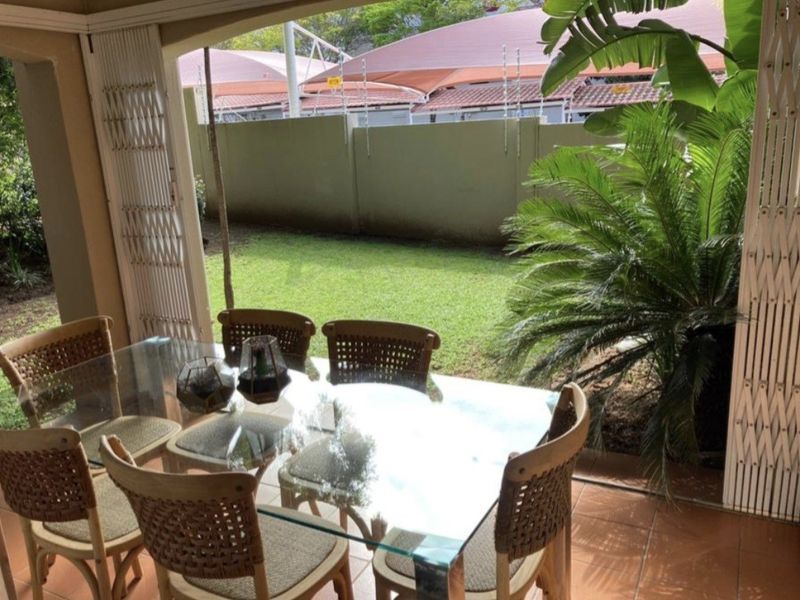 A covered patio area featuring tiled flooring and a security gate, overlooking a private garden space with a perimeter wall.
