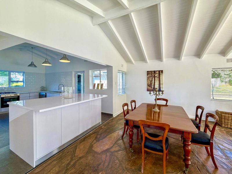 Spacious open-plan kitchen and dining area featuring exposed beam ceilings, a modern kitchen island, and distinctive stone flooring.