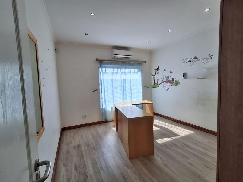 A bedroom featuring laminate flooring, recessed downlights, a split-system air conditioner, and a built-in desk unit.