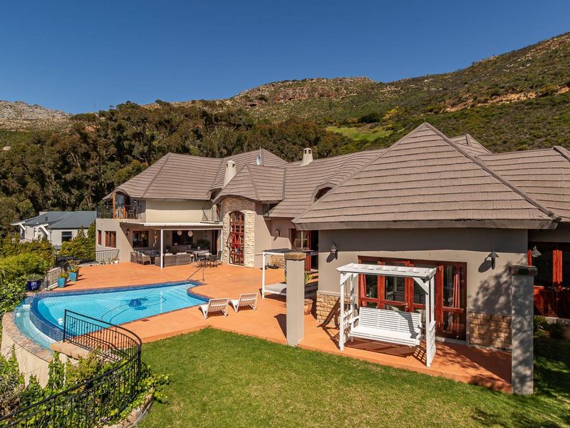 Spacious rear exterior featuring a swimming pool, expansive tiled patio area, and stone-accented facade set against a scenic mountain backdrop.