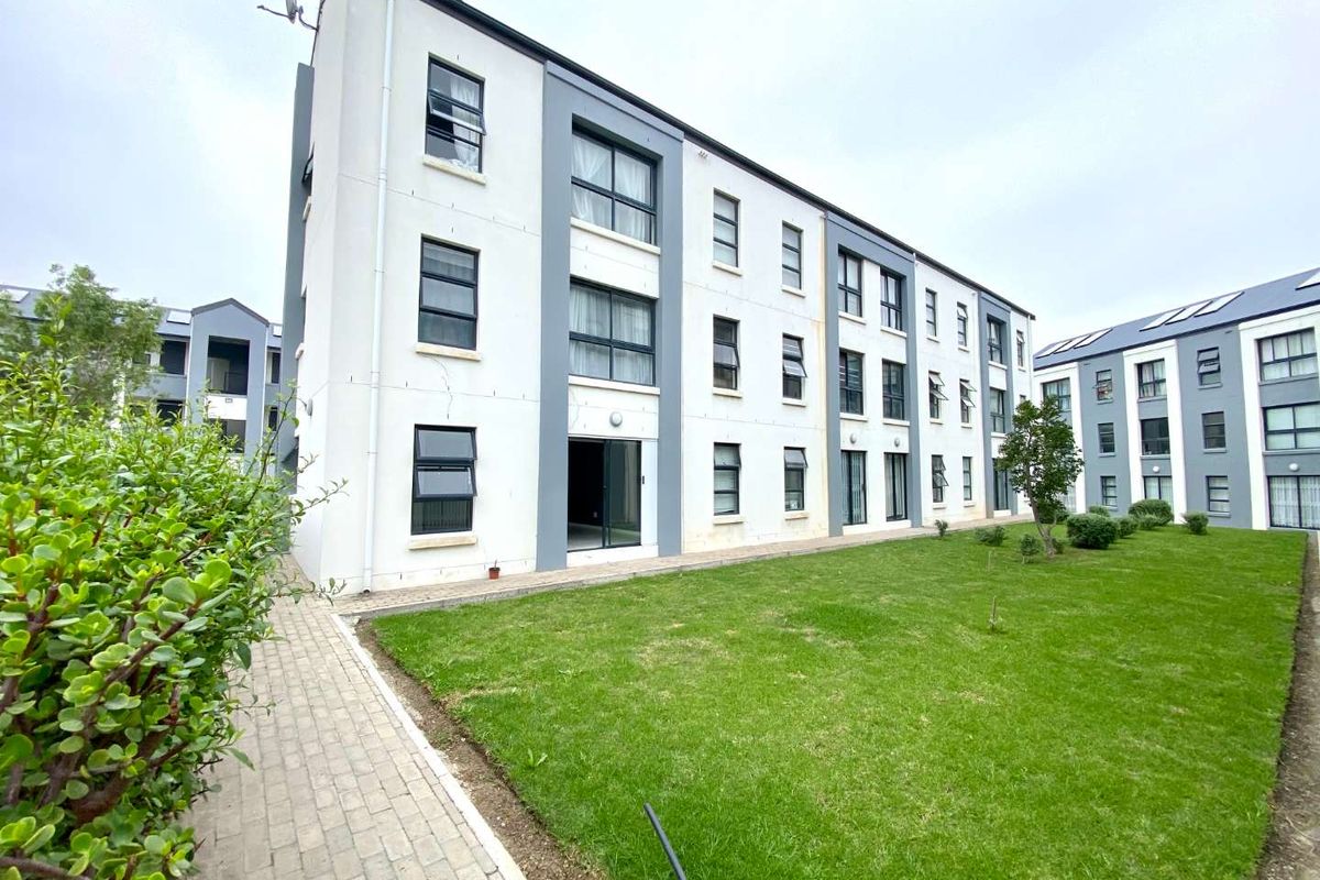 Rear view of a multi-story apartment building featuring a paved walkway and a well-maintained communal lawn area.