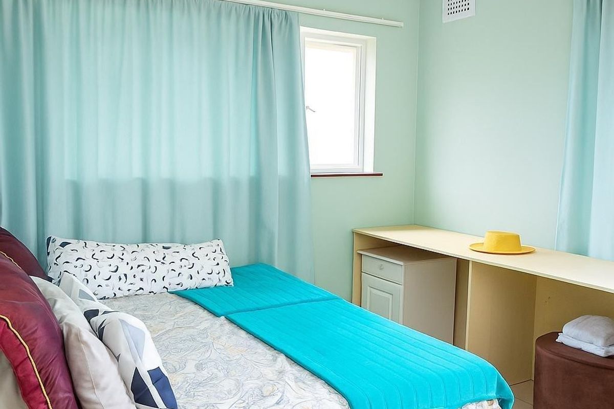 A bedroom featuring exposed timber ceiling beams, light green walls, and a built-in desk area with tiled flooring.