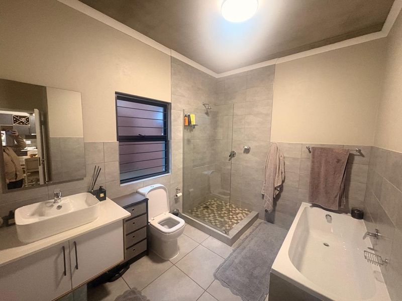 A modern bathroom featuring a vanity with a vessel sink, a separate glass-enclosed shower, and a built-in bathtub with neutral wall and floor tiling.