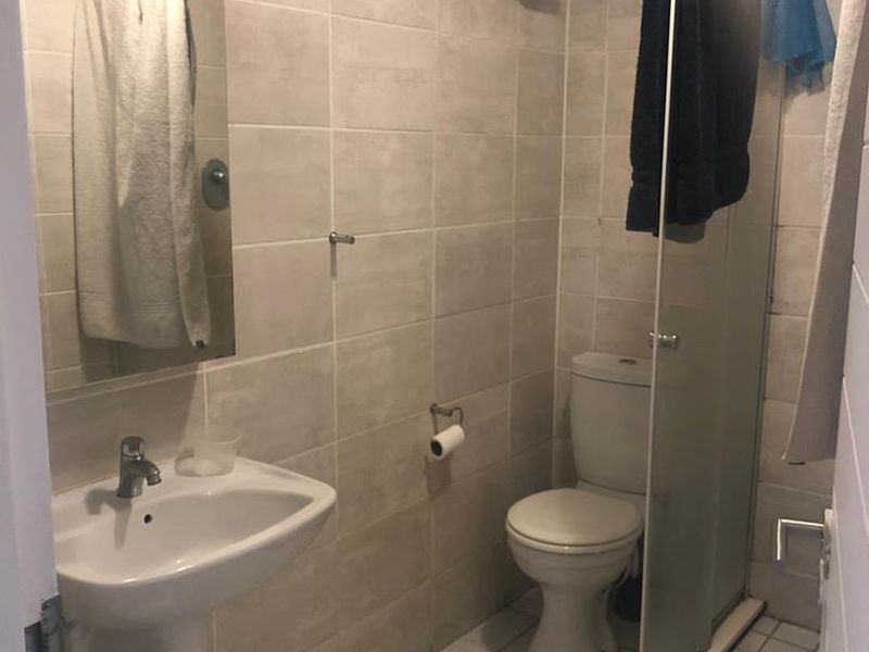 A functional bathroom featuring a pedestal basin, toilet, and a glass-enclosed shower with neutral wall and floor tiling.