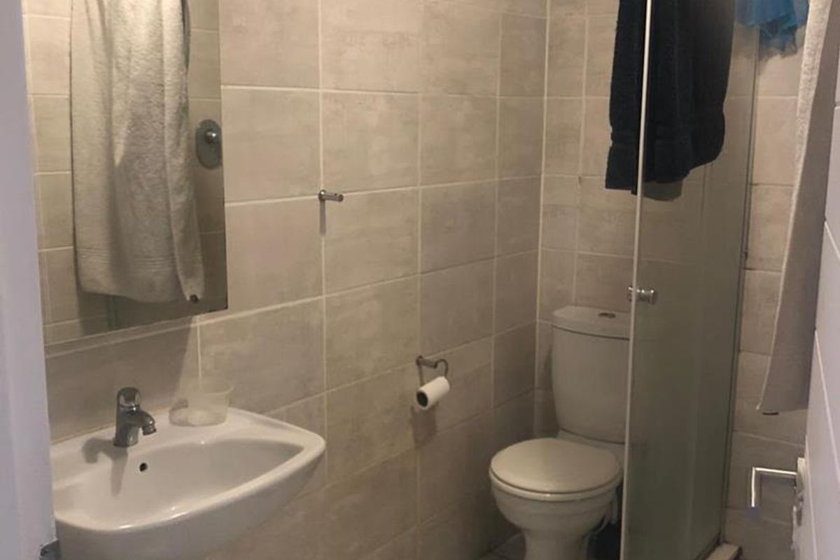 A functional bathroom featuring a pedestal basin, toilet, and a glass-enclosed shower with neutral wall and floor tiling.