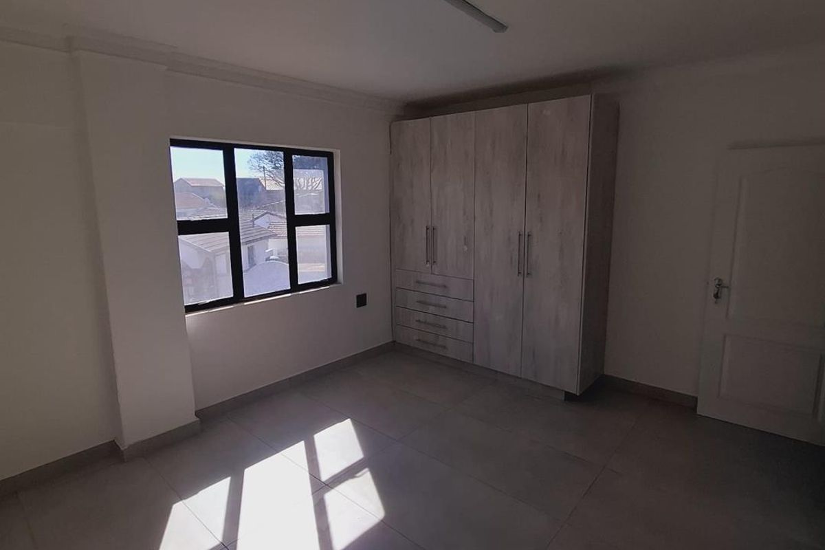 A bright, empty bedroom featuring neutral tiled flooring, built-in cupboards, and a modern aluminium window frame.