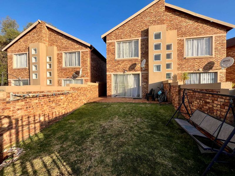 Rear view of a double-storey face brick townhouse featuring a private garden, paved patio area, and sliding door access.