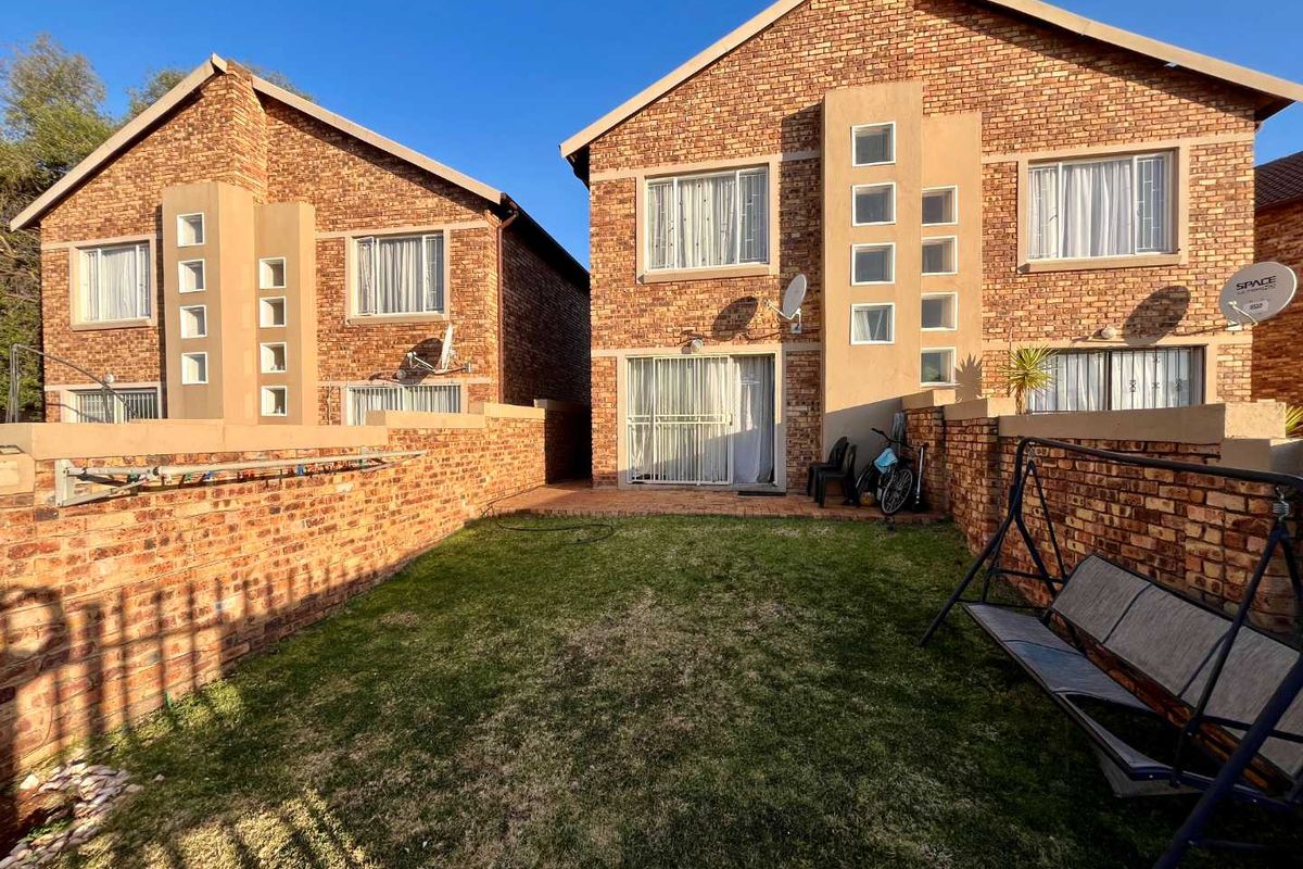 Rear view of a double-storey face brick townhouse featuring a private garden, paved patio area, and sliding door access.