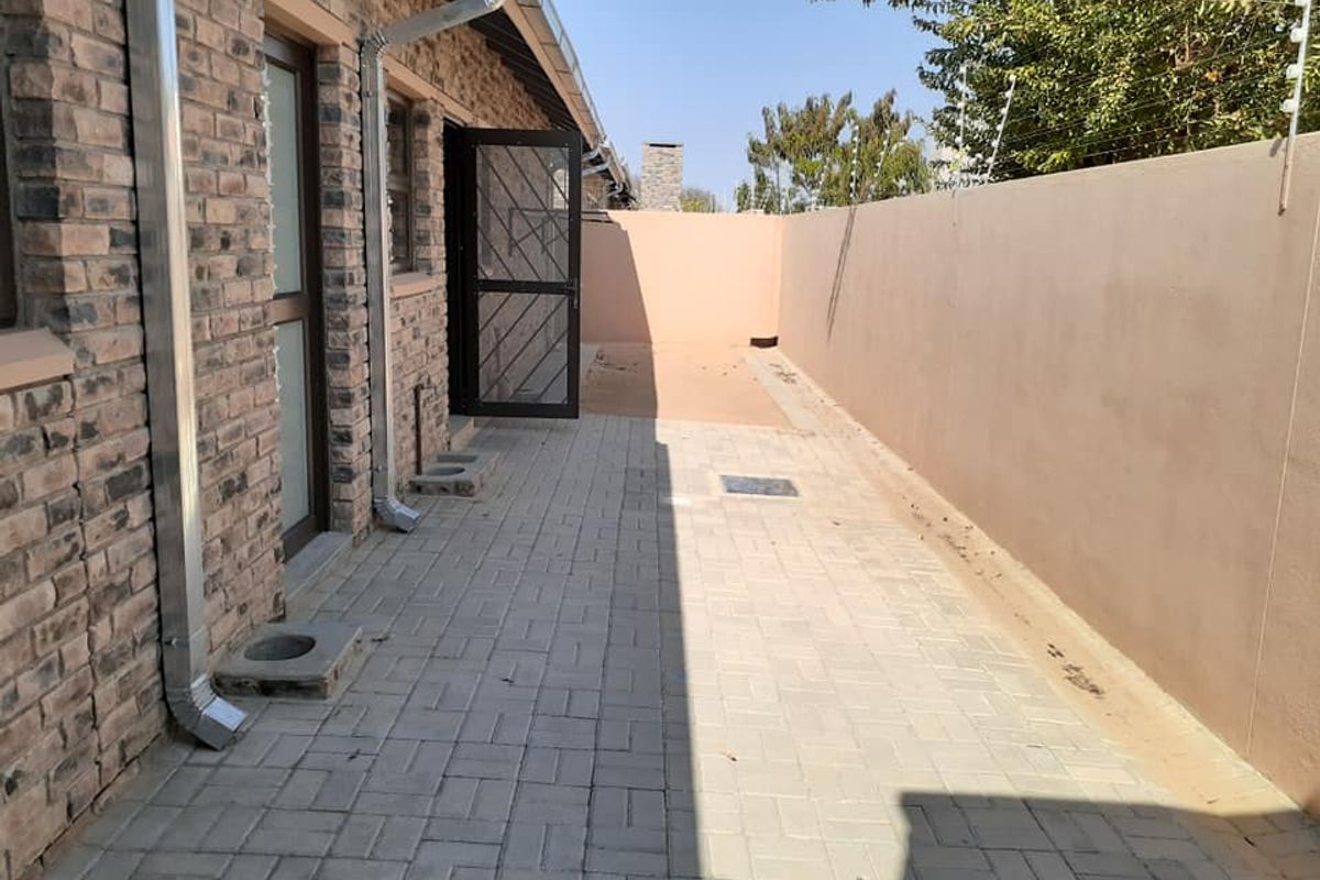 A paved side courtyard area featuring face-brick exterior walls, downpipes, and a high boundary wall with electric fencing.