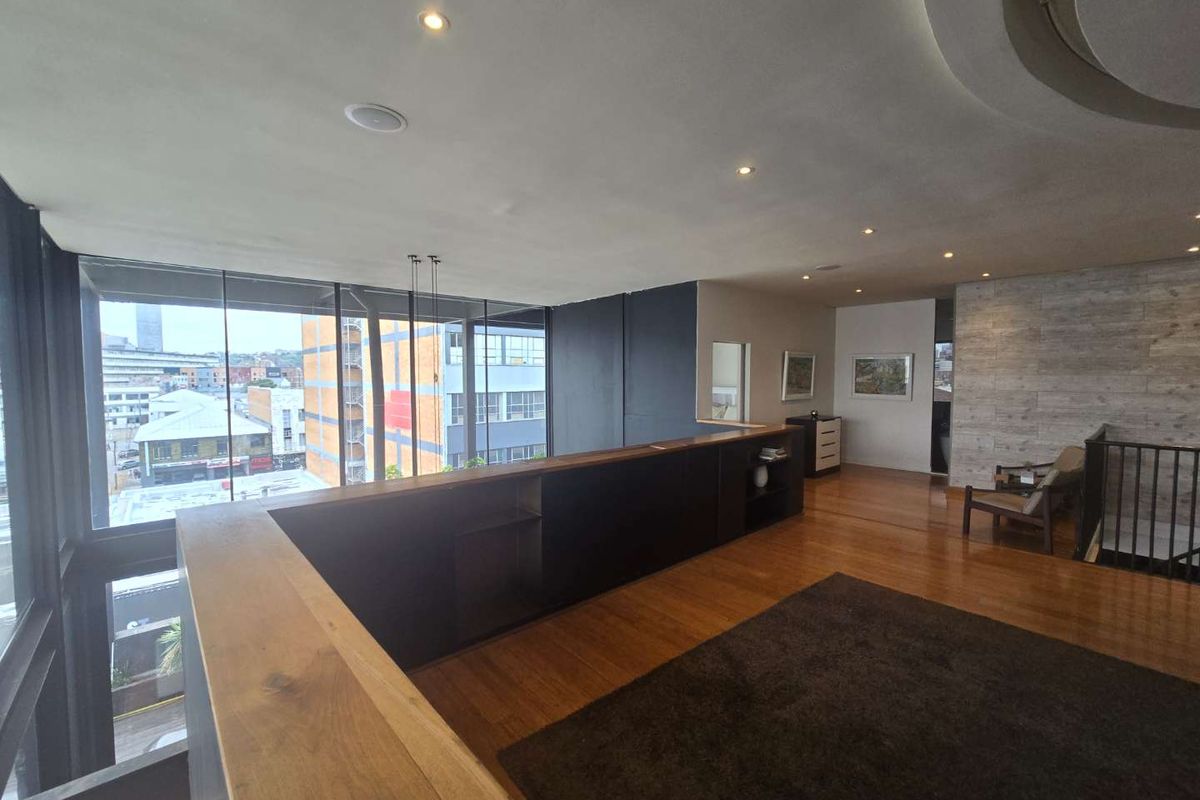 Spacious mezzanine living area featuring hardwood flooring, floor-to-ceiling windows with urban views, and integrated built-in cabinetry.
