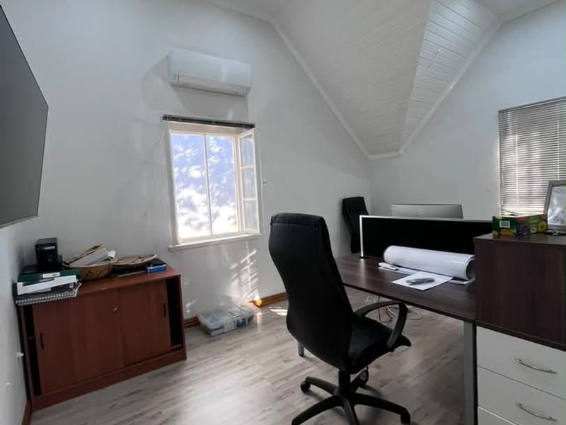 A bright office space featuring a vaulted timber ceiling, laminate flooring, recessed lighting, and a wall-mounted air conditioning unit.