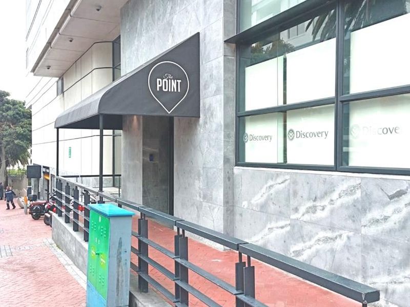 Exterior view of the office building entrance featuring stone cladding, a modern metal awning, and large glass windows along a paved walkway.