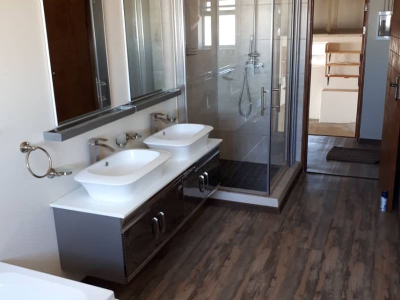 Modern bathroom featuring a double vanity with vessel sinks, a glass-enclosed shower with a rain shower head, and wood-look laminate flooring.