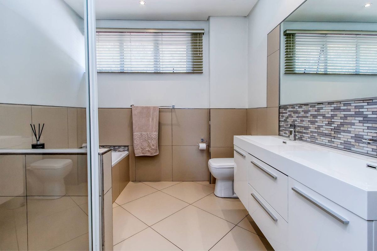 Modern bathroom featuring a sleek white vanity, large wall mirror, tiled shower enclosure, and neutral floor tiling with a built-in bathtub.