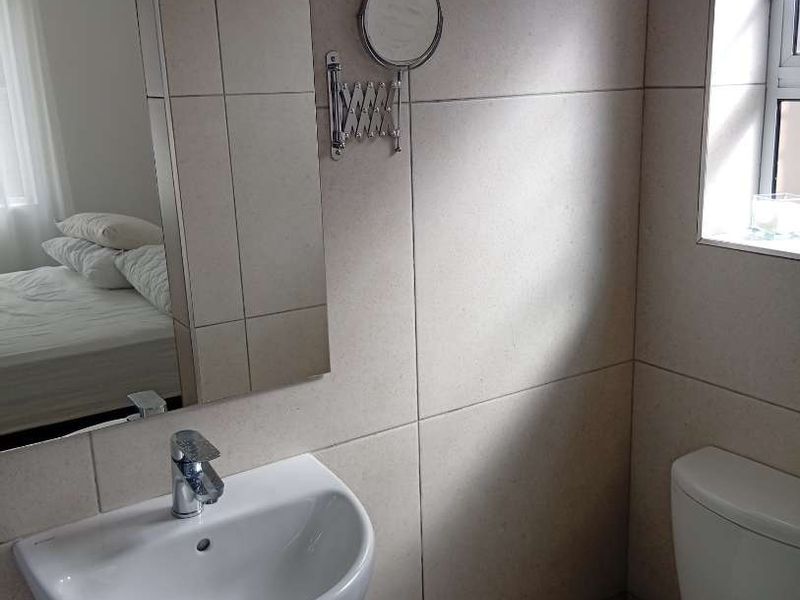 A clean, functional bathroom featuring a wall-mounted basin, chrome fixtures, a wall-mounted mirror, and neutral wall tiling.