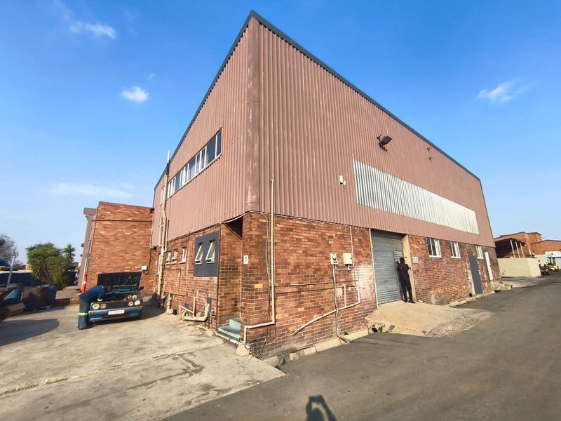 Industrial warehouse building featuring a combination of face brick and corrugated metal cladding with a roller shutter door access point.