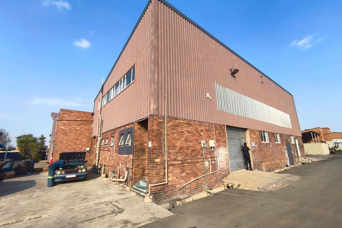 Industrial warehouse building featuring a combination of face brick and corrugated metal cladding with a roller shutter door access point.