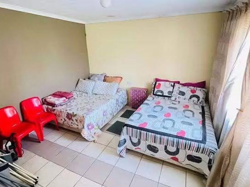 A bedroom featuring tiled flooring and large windows with curtain rails, providing a functional space for sleeping arrangements.