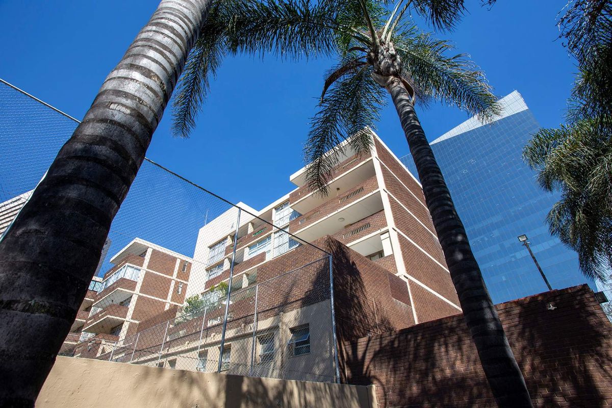 Low angle exterior view of a multi-story brick apartment building featuring private balconies and perimeter security fencing.