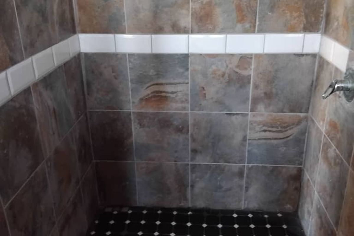 A walk-in shower enclosure featuring decorative slate-style wall tiles, a contrasting black and white mosaic floor, and a chrome shower fixture.