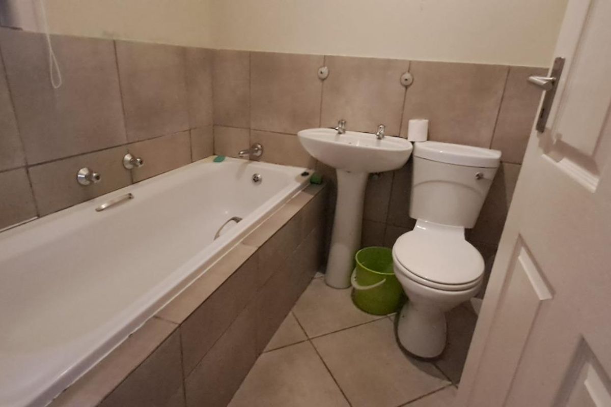 A functional bathroom featuring a built-in bathtub with tiled surround, a pedestal basin, and a standard toilet.