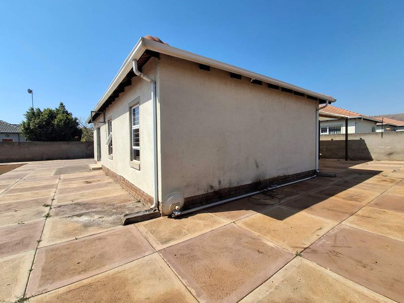 Rear exterior view of the house featuring a large paved patio area, perimeter boundary walls, and standard window fixtures.