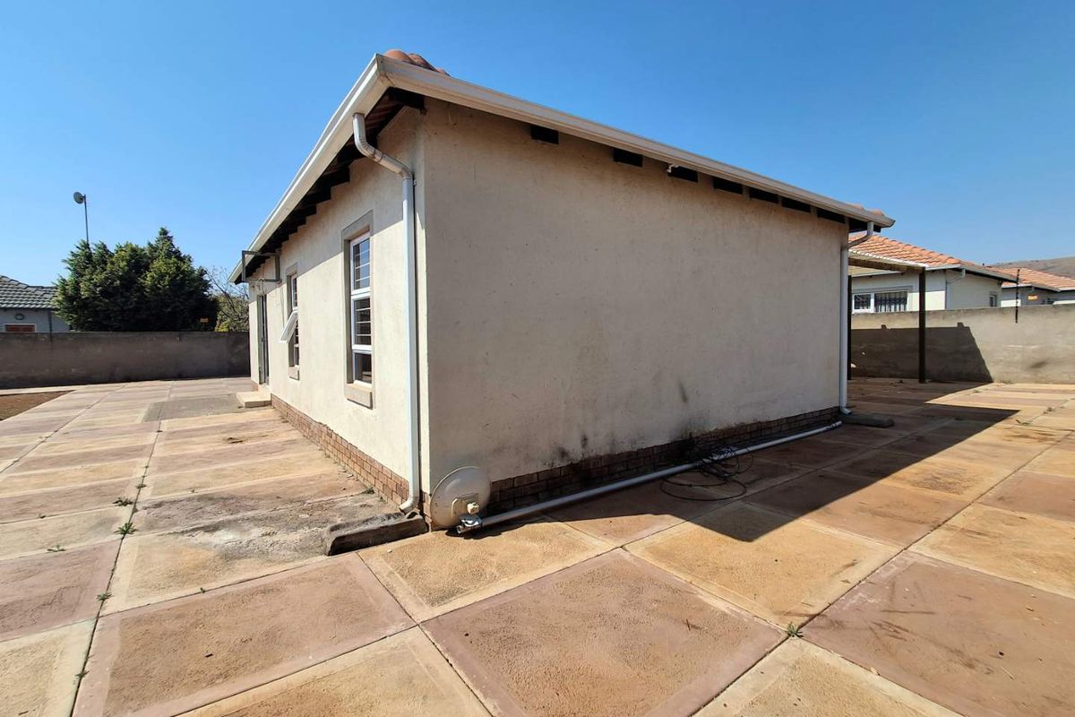 Rear exterior view of the house featuring a large paved patio area, perimeter boundary walls, and standard window fixtures.