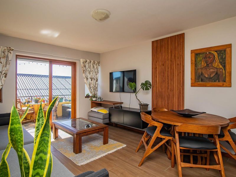 Open-plan living and dining area featuring wood-look tile flooring, vertical wood wall accents, and direct access to an outdoor balcony through sliding glass doors.
