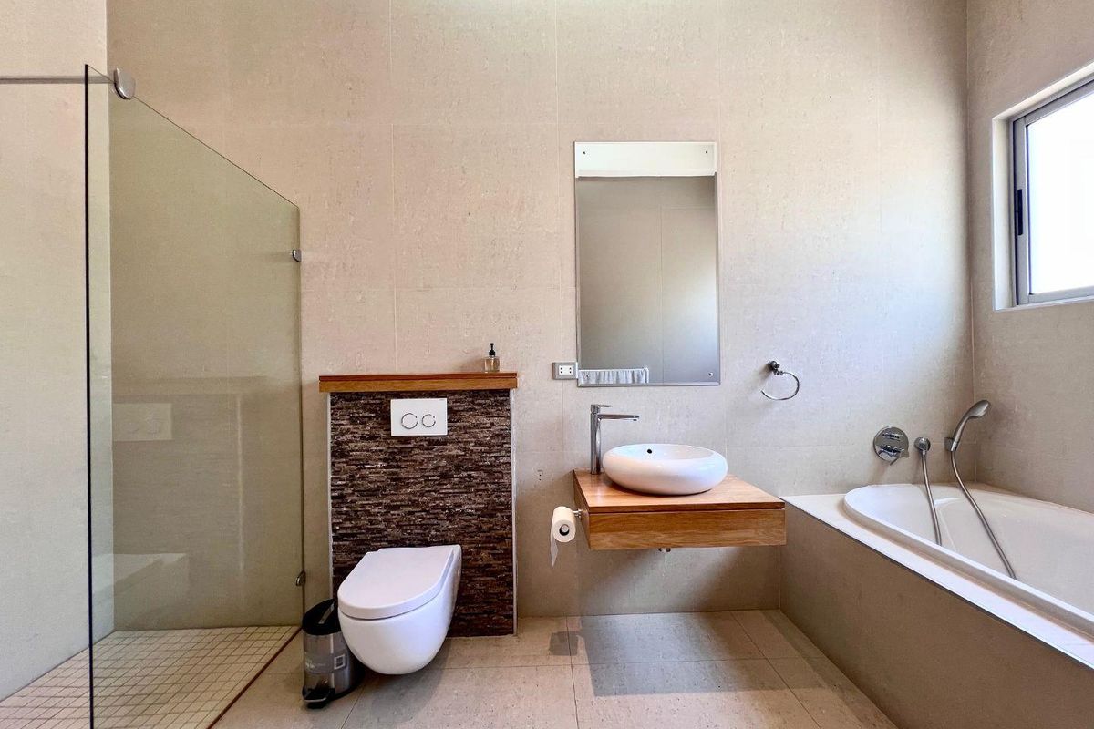 Modern bathroom featuring a wall-mounted vanity with vessel sink, a built-in bathtub, a glass-enclosed walk-in shower, and a wall-hung toilet with tiled feature wall.