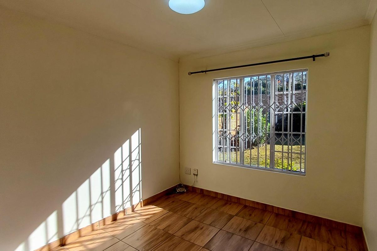 A bright, empty bedroom featuring wood-look tiled flooring and a window fitted with a security gate, offering a clean and neutral living space.