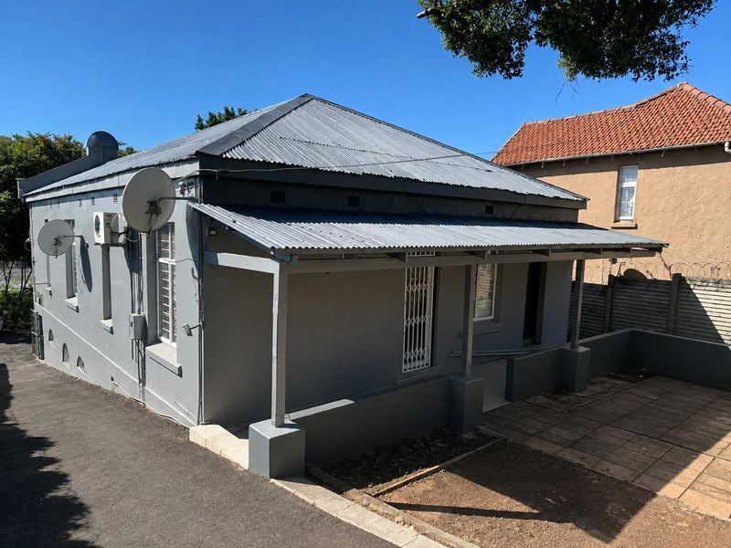 Front elevation of a single-story house featuring a corrugated iron roof, covered veranda, and paved outdoor area.