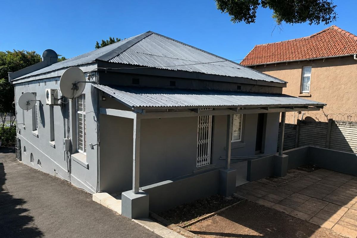 Front elevation of a single-story house featuring a corrugated iron roof, covered veranda, and paved outdoor area.